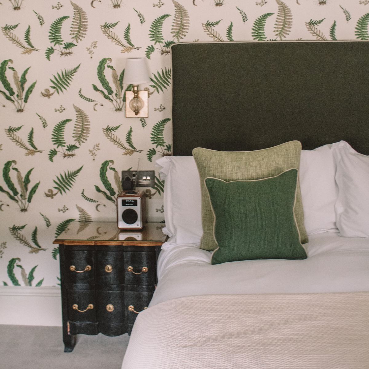Hotel bedroom with fern wallpaper and green velvet headboard