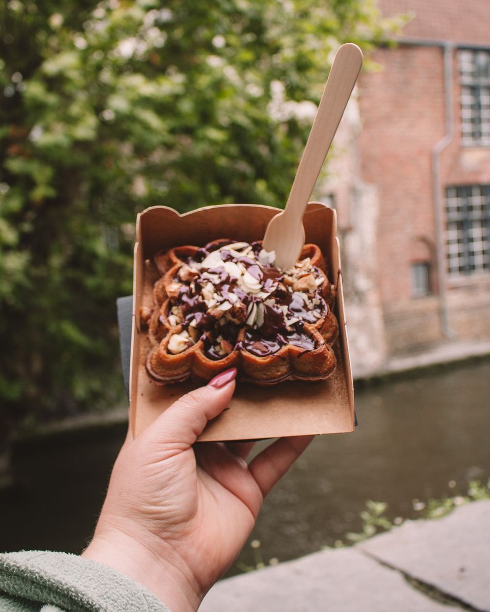 Hand holding a chocolate waffle beside a Bruges canal