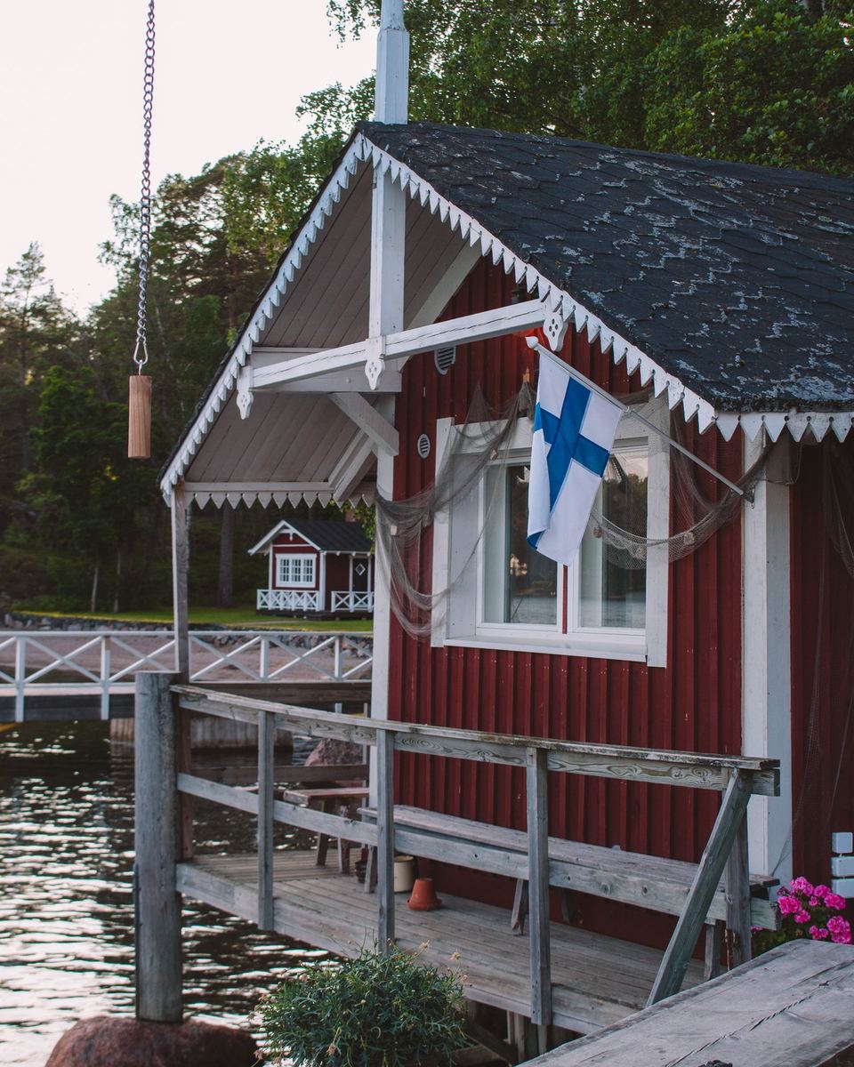 Red wooden cottage with a Finnish flag on the water